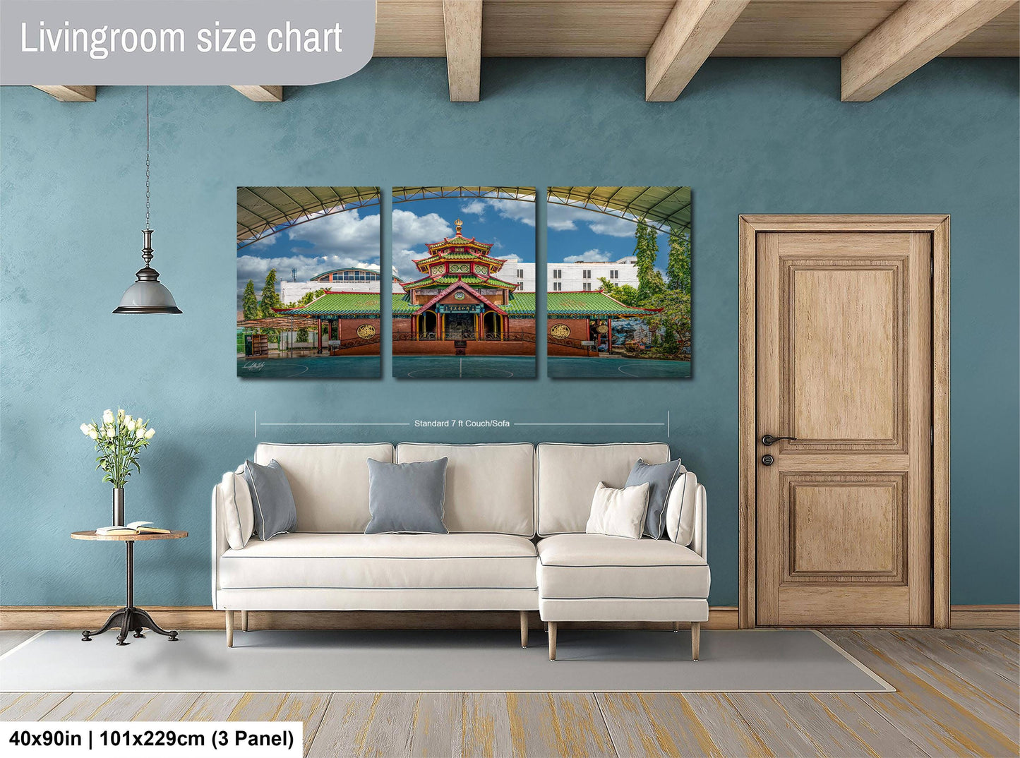 The image is a living room with a large, colorful, and detailed painting of a temple or pagoda hanging on the wall. The painting is divided into three panels, and the wall is painted a light blue color. There is a white sofa and a wooden door in the room.