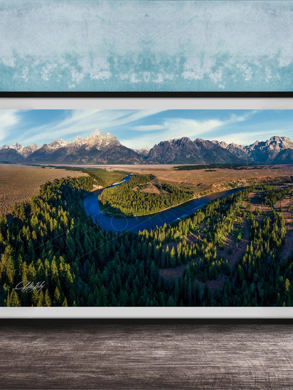 The image is a framed aerial view of a mountainous landscape with a winding river, surrounded by lush forests.