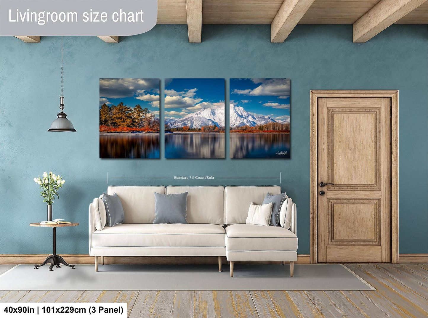 The image is a living room with a large, three-panel landscape painting hanging on the wall. The painting depicts a serene mountain scene with a lake and trees. The room has a white sofa and a wooden door, creating a cozy and inviting atmosphere.