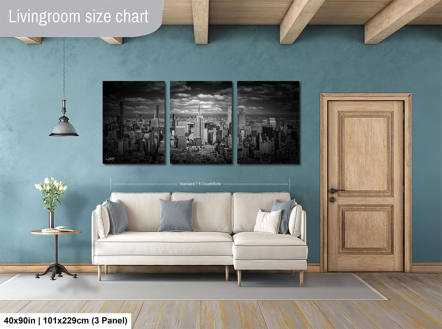 The image is a living room with a large, three-panel black and white cityscape painting hanging on the wall. The painting is approximately 40 inches wide and 101.29 centimeters tall. The room also includes a white sofa, a wooden door, and a small table with a vase of flowers.
