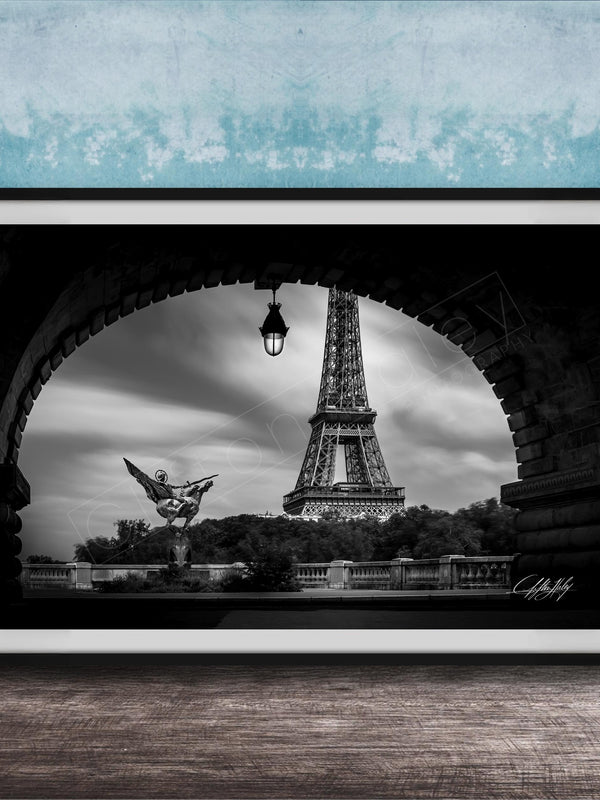 A black and white photograph of the Eiffel Tower in Paris, France, framed and displayed on a wooden surface against a blue textured wall.