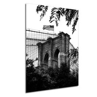 A black and white photograph of the Brooklyn Bridge, with the American flag flying atop the structure.
