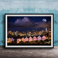 A framed photograph of a city skyline at night, with a full moon in the sky and colorful houses lining the streets.