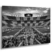 A black and white photograph of a football stadium during a game, with a large crowd of spectators filling the stands.