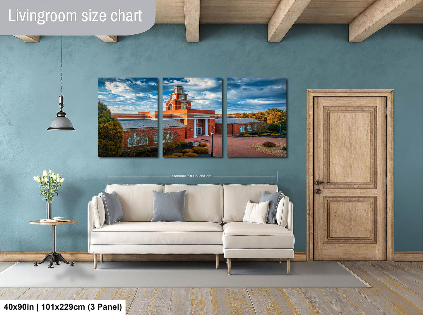 The image is a living room with a white sofa and a wooden door. Above the sofa, there is a large painting depicting a building with a tower. The painting is divided into three panels, each showing different parts of the building. The wall behind the sofa has a blue color, and there is a lamp hanging from the ceiling. The image is described as a living room size chart, indicating that it is a representation of the actual size of the living room.