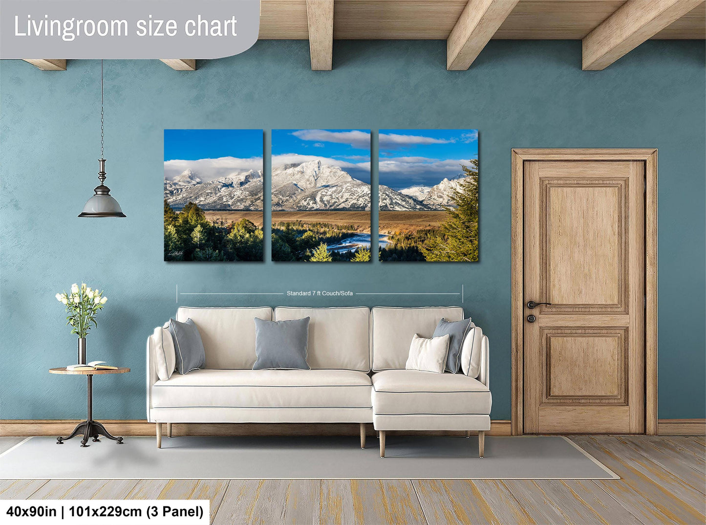 The image is a living room with a large, three-panel landscape painting hanging on the wall. The painting depicts a scenic mountain landscape with snow-capped peaks, a river, and lush green trees. The room has a white sofa and a wooden door, creating a cozy and inviting atmosphere.