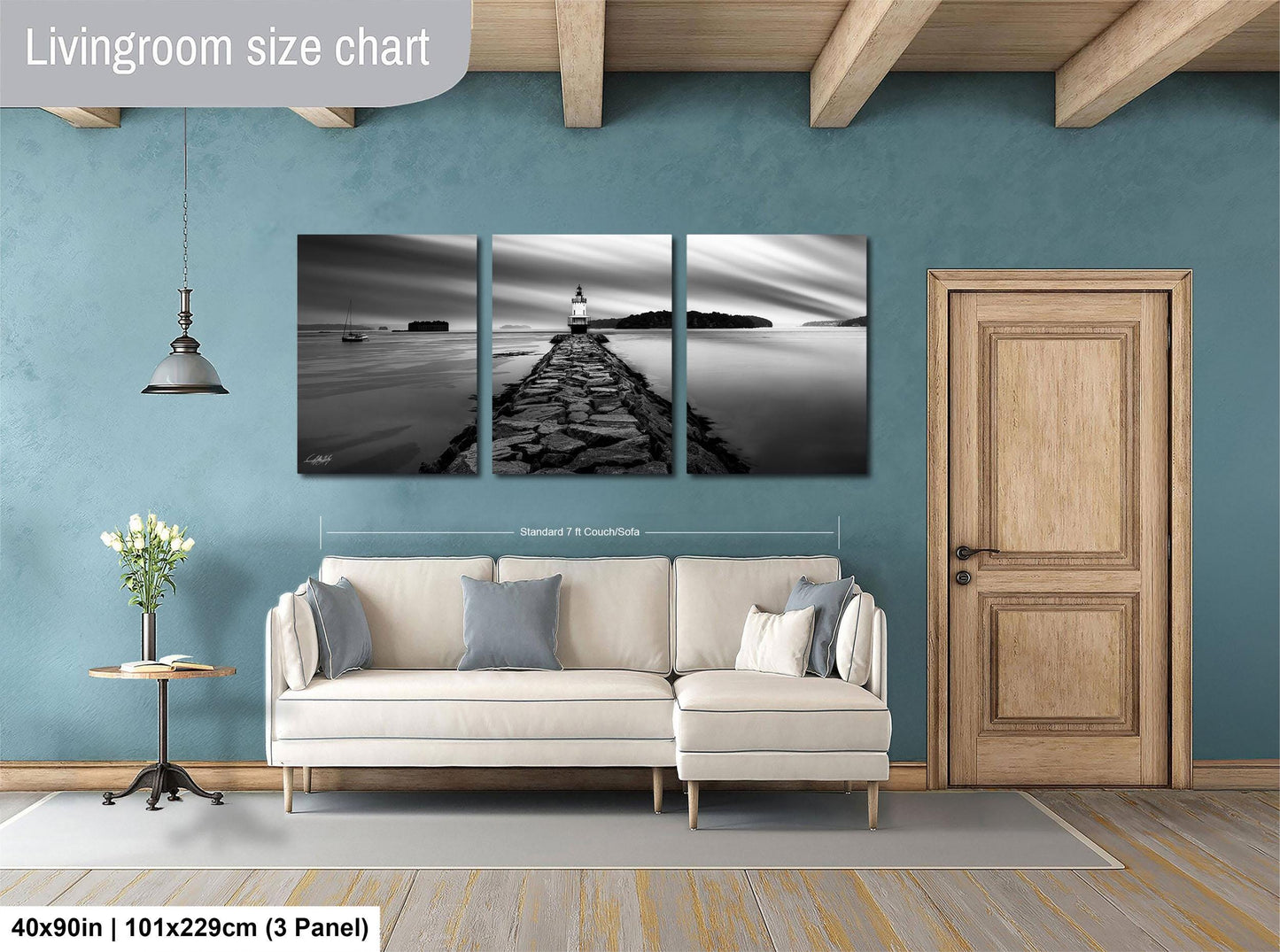 The image is a living room with a large, white sofa and a wooden door. Above the sofa, there is a black and white triptych artwork depicting a lighthouse on a rocky shoreline. The artwork is framed and hangs on the wall, creating a focal point in the room.