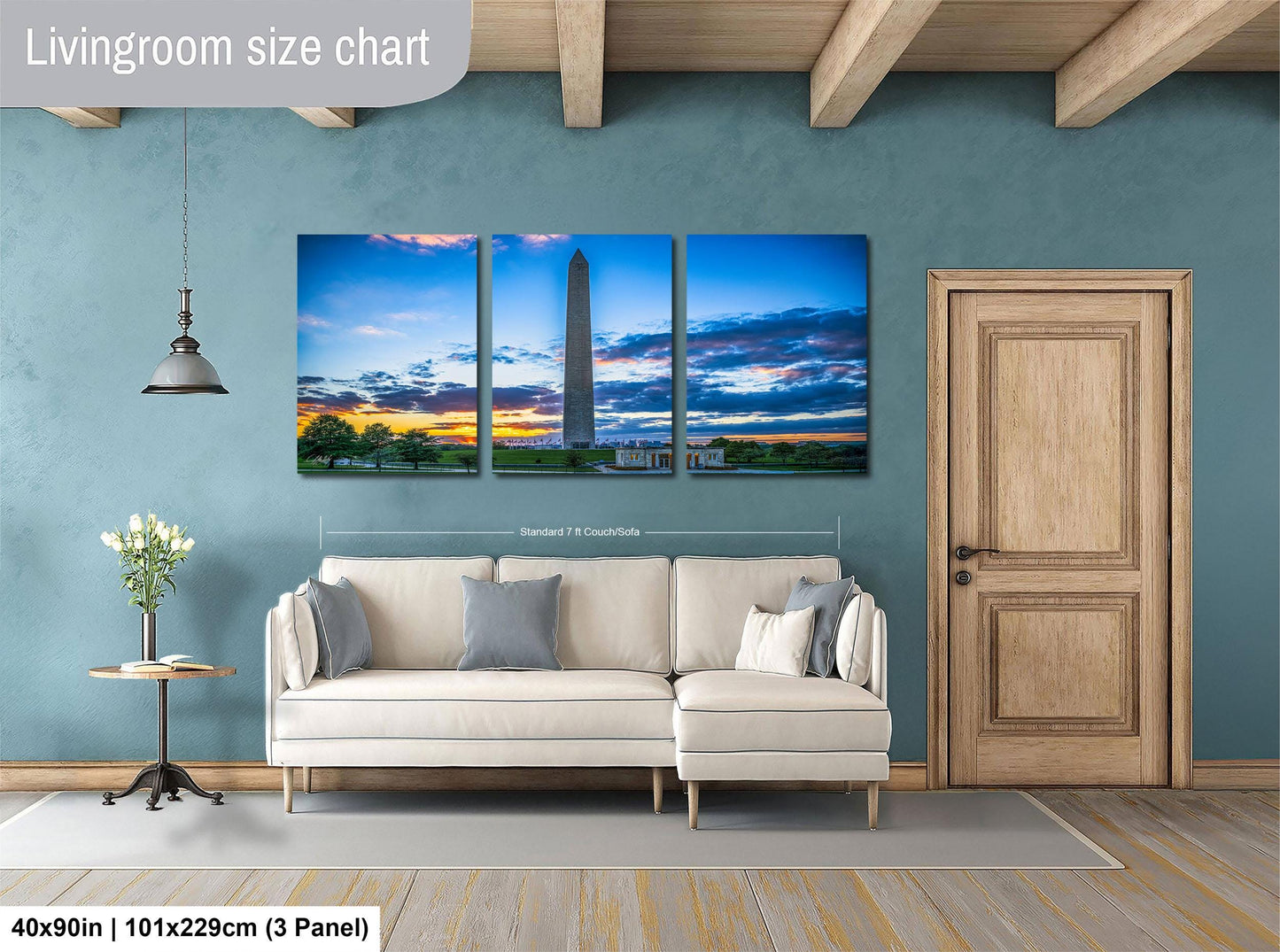 The image is a living room with a large, three-panel wall art depicting a scenic view of the Washington Monument at sunset. The wall art is mounted above a white sofa, and there is a wooden door and a small table with a vase of flowers in the room.