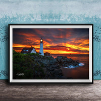 A framed photograph depicting a lighthouse on a rocky cliff at sunset, with the sky filled with vibrant orange and red hues.