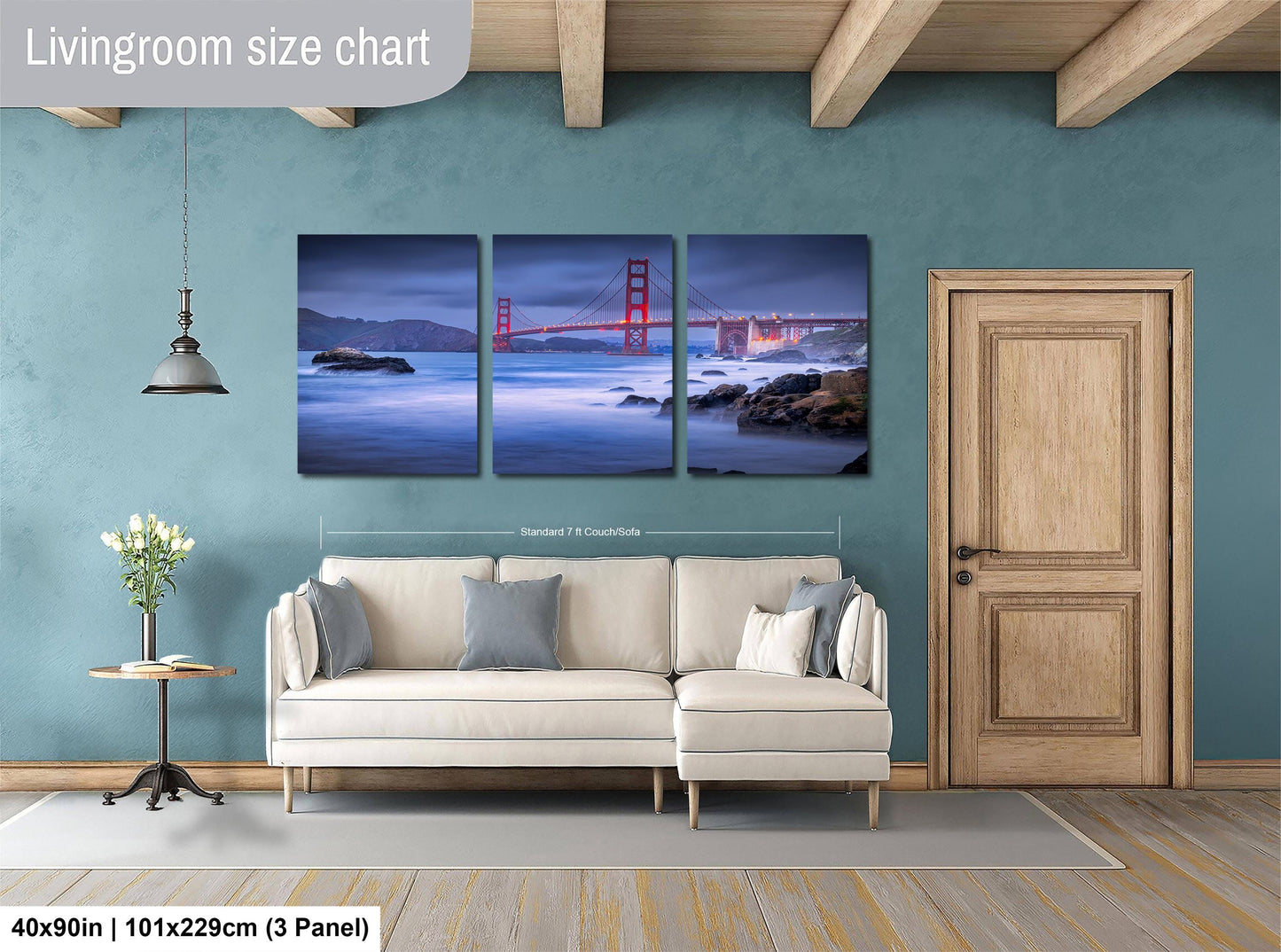 The image is a living room with a large wall art depicting the Golden Gate Bridge at night. The wall art is divided into three panels, with the top and bottom panels showing the bridge and the middle panel showing the ocean. The living room has a white sofa and a wooden door, and the floor is covered with a gray rug.