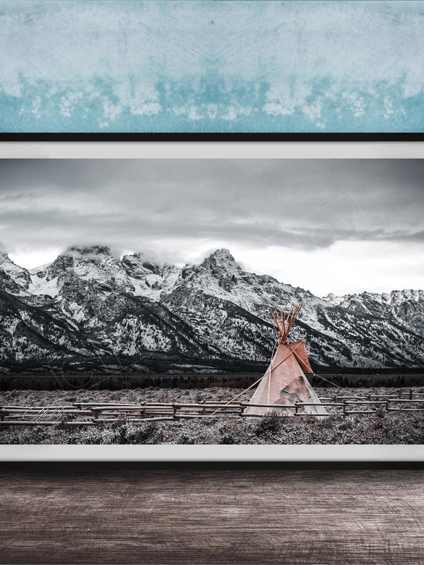 A framed photograph of a teepee in a snowy mountain landscape, with a blue wall in the background.