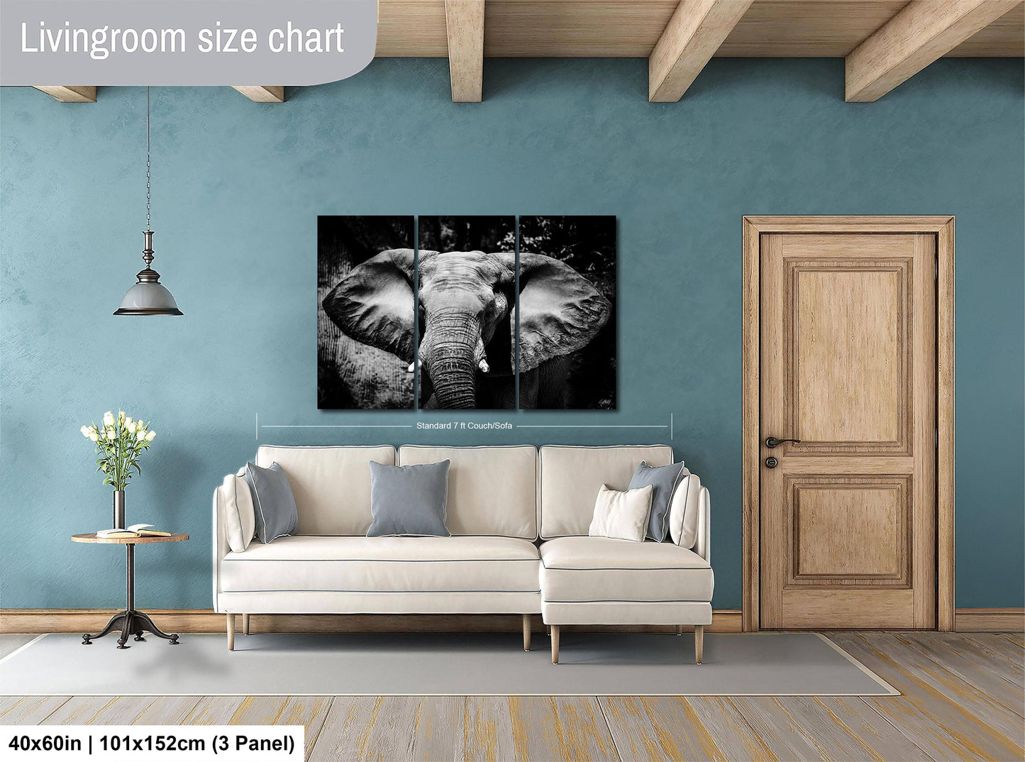 a living room with a large black and white elephant painting hanging on the wall. The painting is framed and measures 40 inches by 101 inches, with a 3-panel layout. The room has a white sofa, a wooden door, and a small table with a vase of flowers.