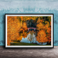 A framed photograph depicting a scenic autumn landscape with a red bridge spanning a tranquil lake surrounded by vibrant orange and yellow foliage.