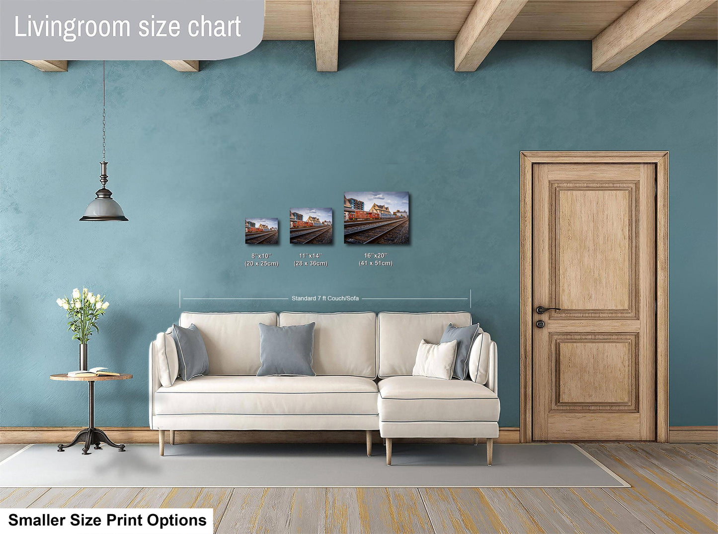 a living room with a white sofa, a wooden door, and a hanging light fixture. There are three framed pictures of train tracks on the wall, and the text indicates that the living room is designed for smaller print options.