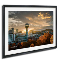 a city skyline at sunset, with a large tower in the center and a mix of buildings surrounding it. The sky is filled with clouds, creating a dramatic backdrop for the cityscape.