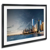 A framed photograph of the New York City skyline, with the One World Trade Center prominently visible against a cloudy sky.