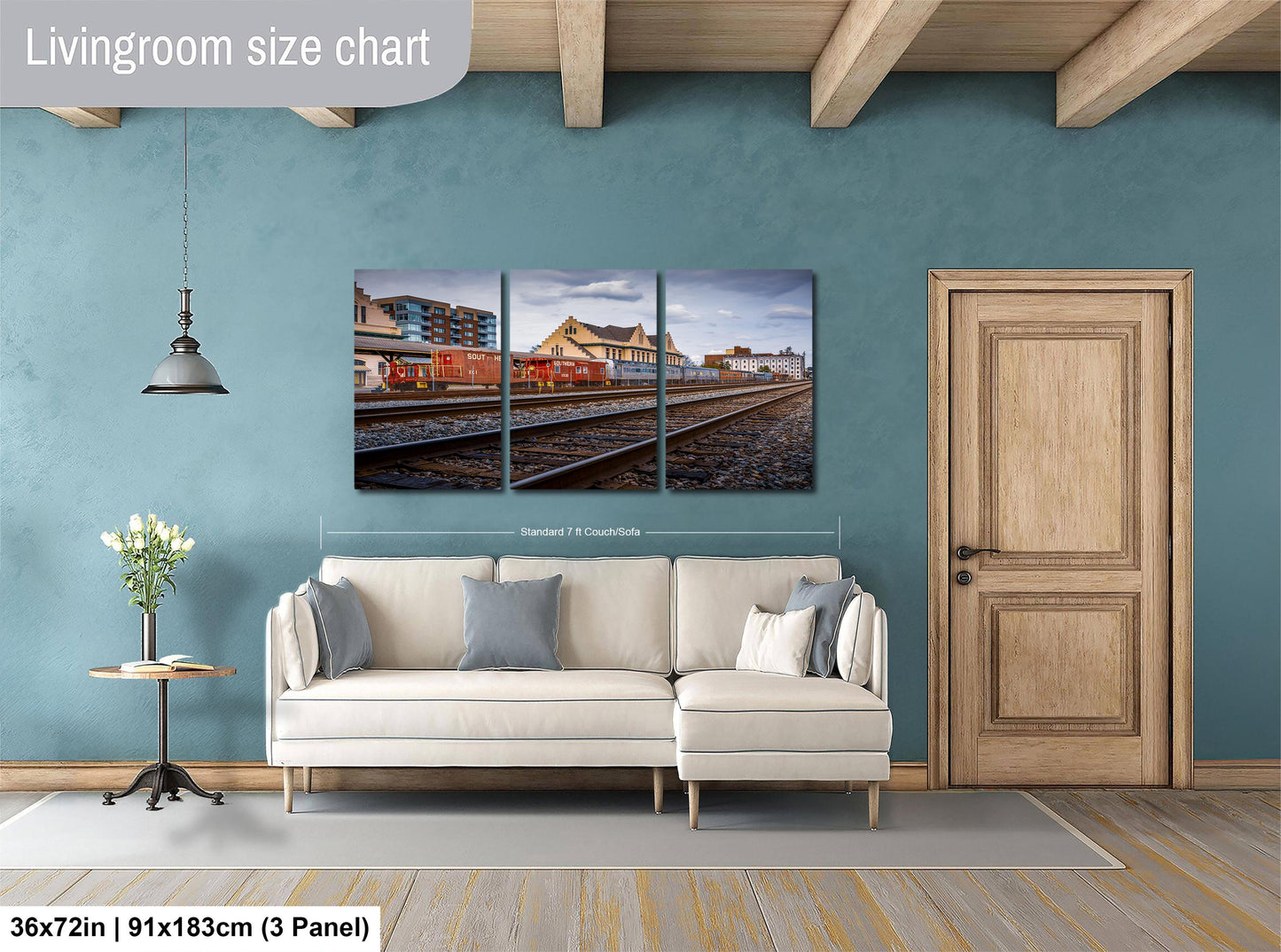 The image is a living room with a large white sofa, a wooden door, and a painting of a train station on the wall.