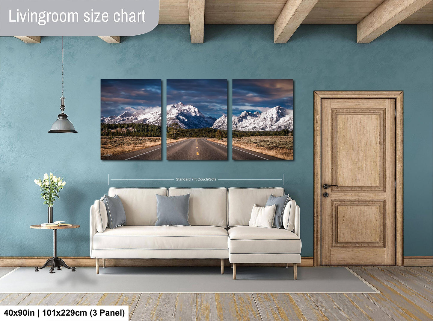 The image is a living room with a large wall art piece depicting a scenic mountain road. The art piece is divided into three panels, each showing a different stage of the road. The living room has a white sofa and a wooden door, creating a cozy and inviting atmosphere.