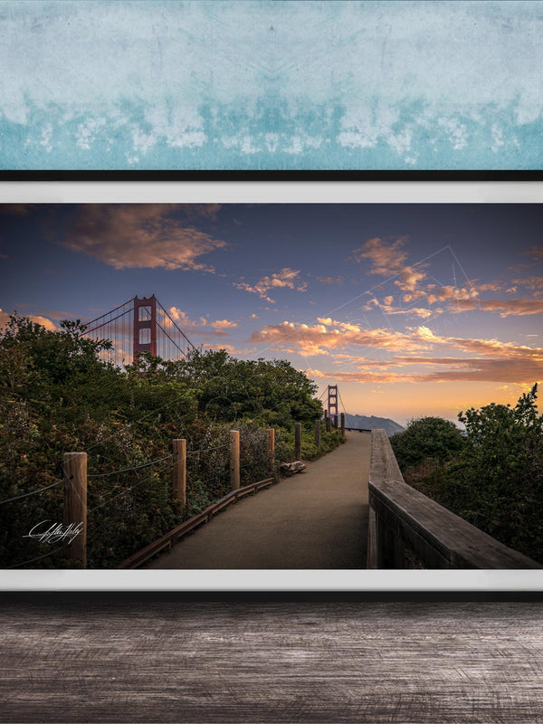 A framed photograph depicting a scenic view of the Golden Gate Bridge at sunset, with a wooden walkway leading towards the bridge and a colorful sky in the background.