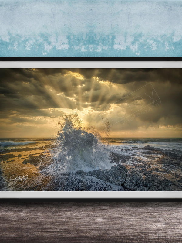 The image is a framed photograph of a dramatic ocean scene, with crashing waves and a dramatic sky filled with clouds and sunbeams.