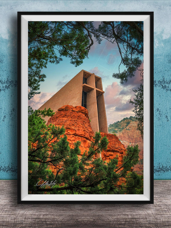 A framed photograph of a large, modern church with a distinctive cross-shaped roof, set against a backdrop of red rock formations and lush greenery.