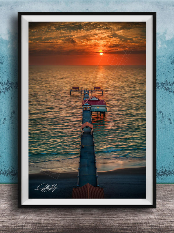 A framed photograph depicting a serene sunset over a body of water, with a pier extending into the water and a small building on the pier.