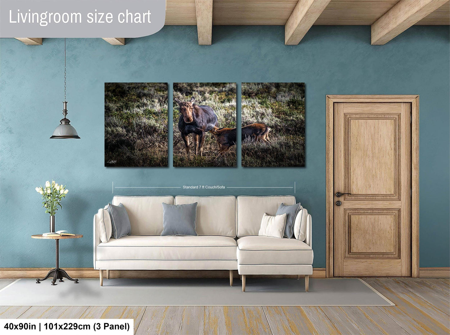 The image is a living room with a large white sofa, a wooden door, and a hanging light fixture. Above the sofa, there is a triptych of animal photographs, including a moose and a deer, displayed on the wall.