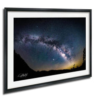 a stunning night sky with a galaxy and stars, framed in a black frame and hung on a wall.