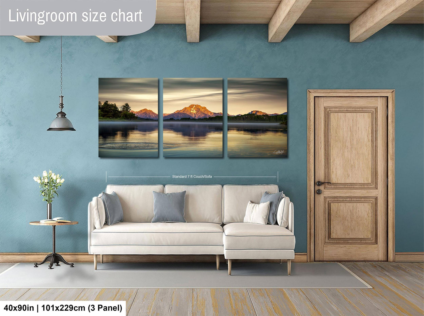 The image is a living room with a large, three-panel landscape painting hanging on the wall. The painting depicts a serene mountain lake scene with a sunset over the water. The room is furnished with a white sofa and a wooden door, creating a cozy and inviting atmosphere.