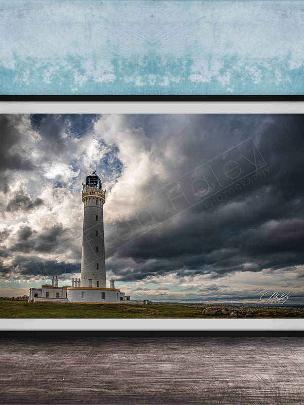 A framed photograph of a lighthouse against a stormy sky, with the lighthouse standing tall on a grassy field.