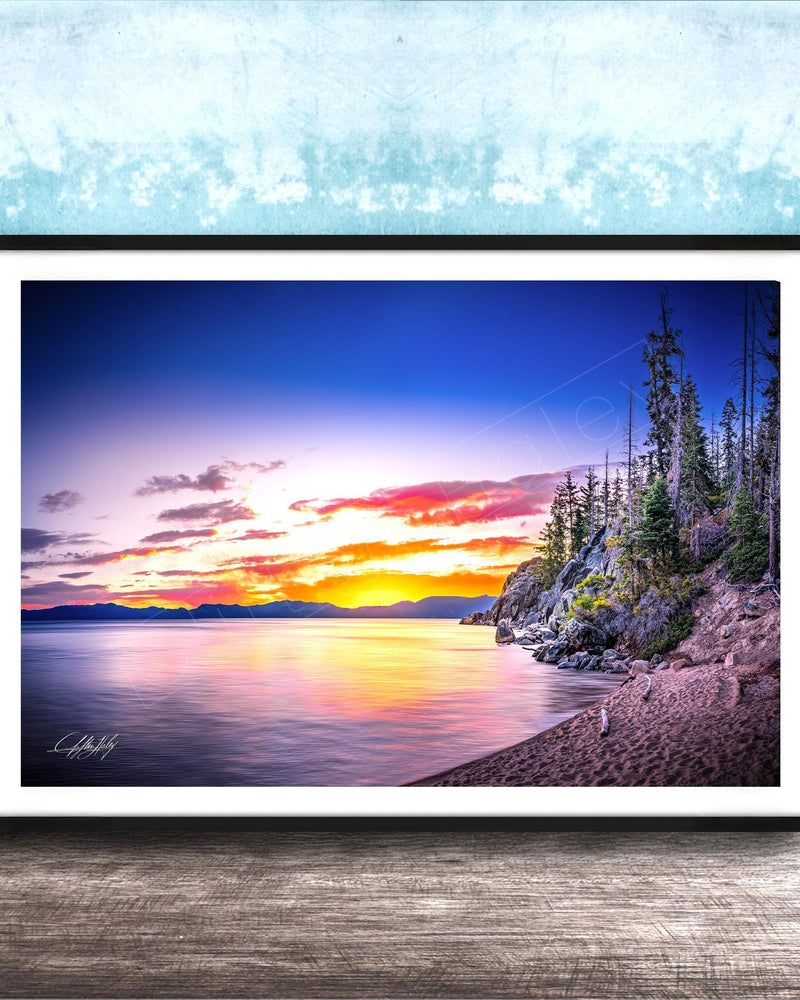 A framed photograph depicting a serene landscape with a calm lake reflecting the vibrant colors of a sunset sky, surrounded by trees and mountains.