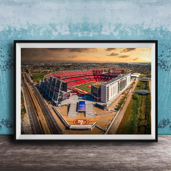 The image is an aerial view of a large sports stadium, likely the 49ers stadium, with its distinctive red roof and surrounding landscape.