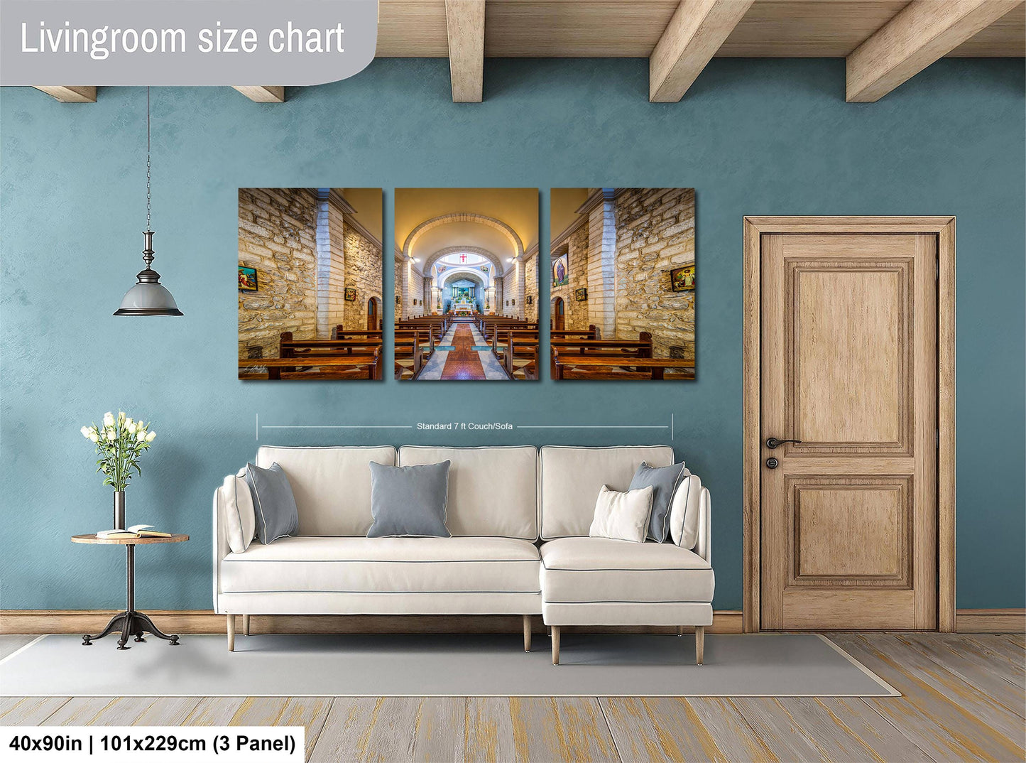 The image is a living room with a large white sofa, a wooden door, and a pendant light. Above the sofa, there is a triptych of paintings depicting a church interior with arched doorways and wooden pews. The wall behind the sofa is painted a light blue color, and the floor is covered with a gray rug. The image is described as a living room size chart, indicating that it is a standard size for a living room.