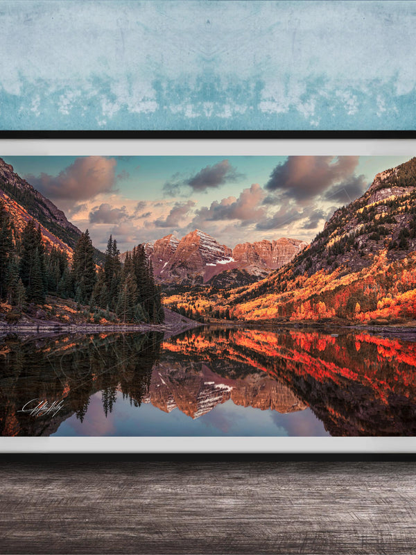 The image is a framed photograph depicting a scenic mountain landscape with a lake reflecting the mountains and trees.