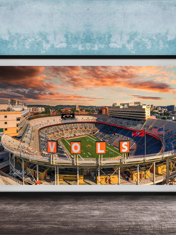 A framed photograph of a sports stadium with the word "VOLS" prominently displayed, set against a backdrop of a colorful sunset sky.