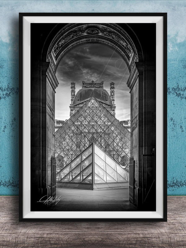 A framed photograph of the Louvre Museum in Paris, France, with the iconic glass pyramid structure prominently featured in the center of the frame.