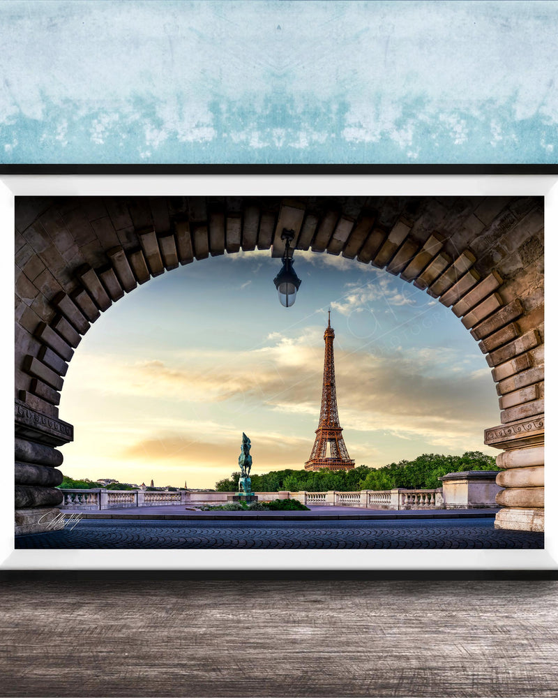 the Eiffel Tower, a famous landmark in Paris, France, captured through an archway. The photograph is framed and displayed on a wooden surface, creating a visually appealing composition.