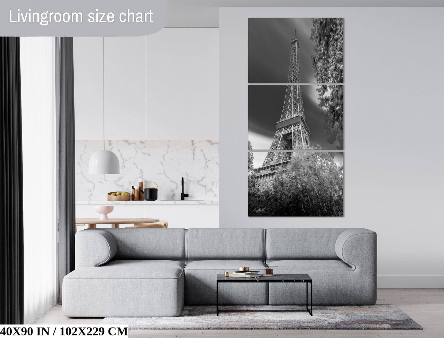The image is a living room with a gray sofa, a coffee table, and a large black and white photograph of the Eiffel Tower on the wall.