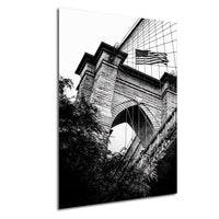 A black and white photograph of a brick bridge with an American flag flying above it, set against a backdrop of trees and foliage.