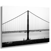 A black and white photograph of a suspension bridge with a long, curved deck and tall, slender towers.