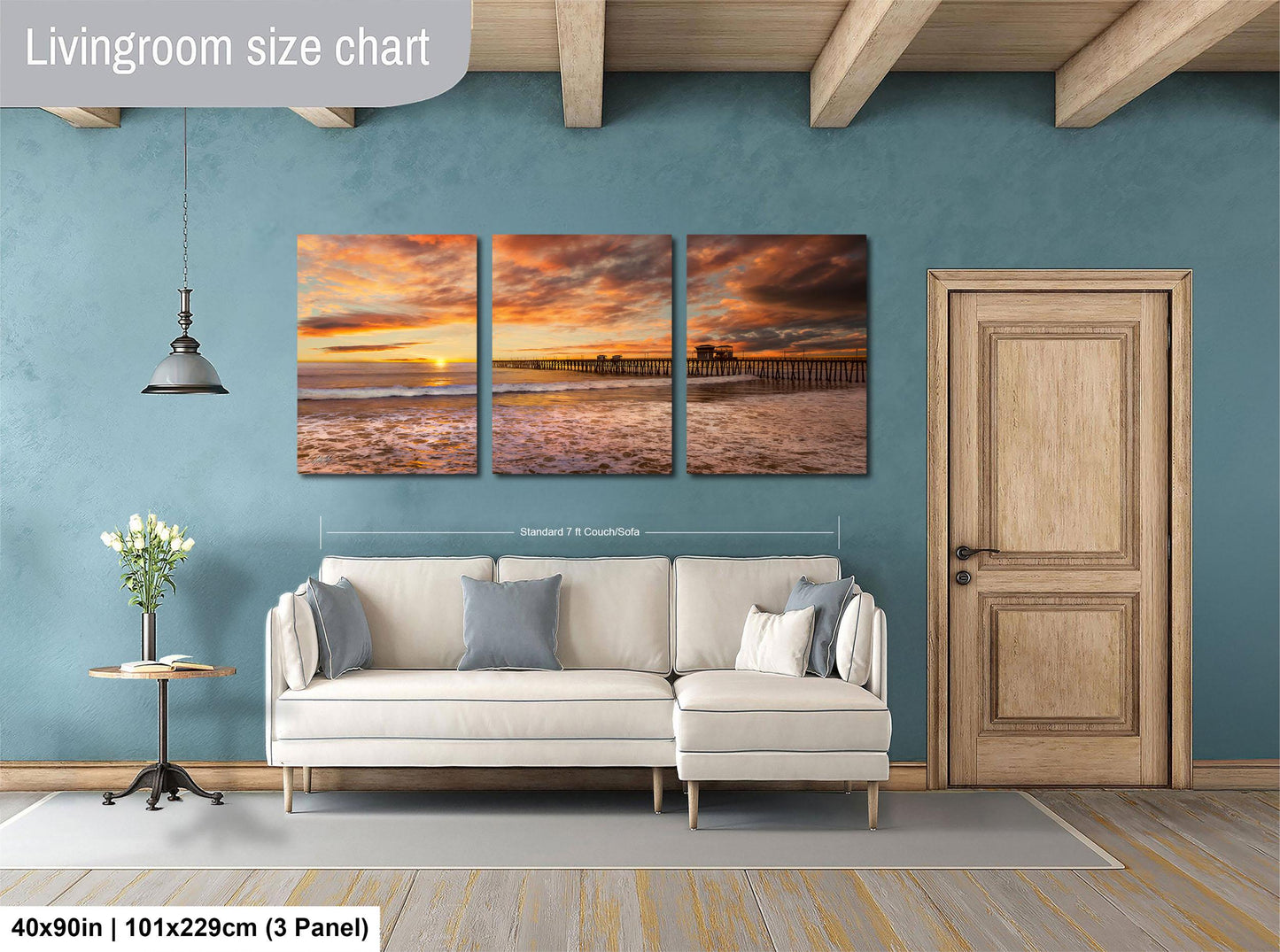 The image is a living room with a large wall art piece depicting a serene beach scene at sunset. The art piece is divided into three panels, each showing different aspects of the beach and sky. The living room has a white sofa and a wooden door, creating a cozy and inviting atmosphere.