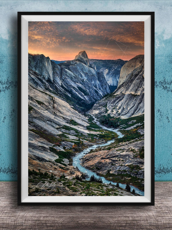 The image is a framed photograph of a mountainous landscape with a winding river, set against a backdrop of a dramatic sky with clouds and a sunset.