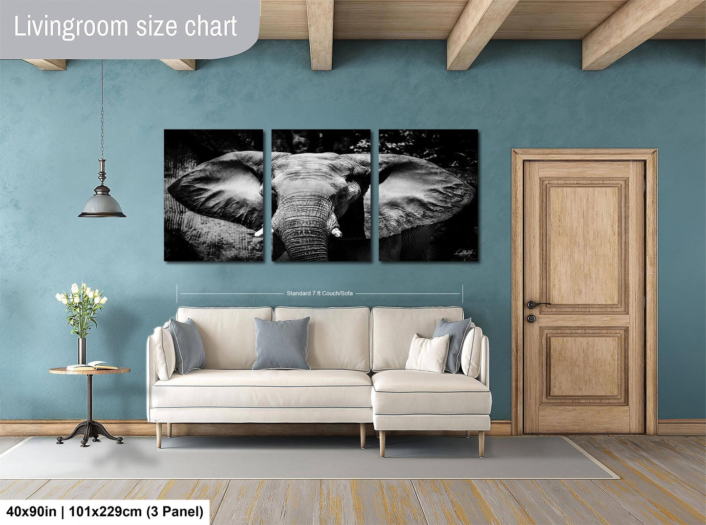 The image is a living room with a large wall art piece depicting an elephant. The wall art is divided into three panels, with the largest panel covering the entire wall. The room features a white sofa, a wooden door, and a small table with a vase of flowers. The living room appears to be well-lit and spacious, with a wooden ceiling and a wooden floor.