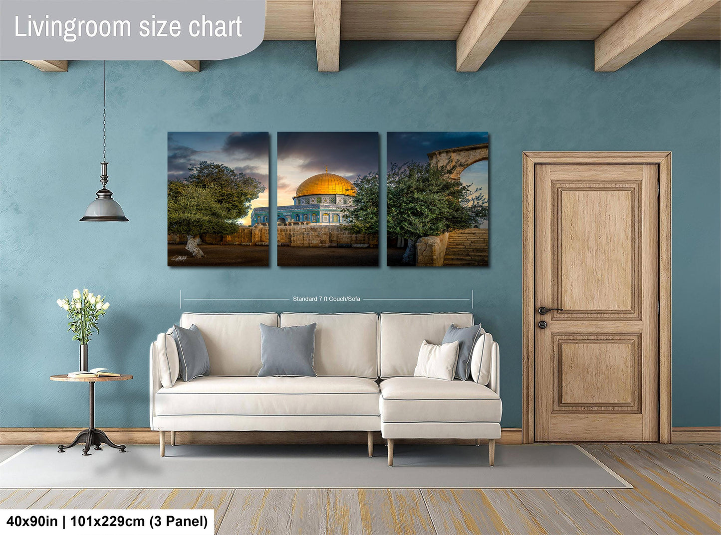 The image is a living room with a white sofa and a wooden door. Above the sofa, there is a triptych of pictures depicting a building and a landscape. The wall behind the sofa has a blue color, and there is a lamp hanging from the ceiling. The image is described as a living room size chart, which means it provides a visual representation of the dimensions of the living room.