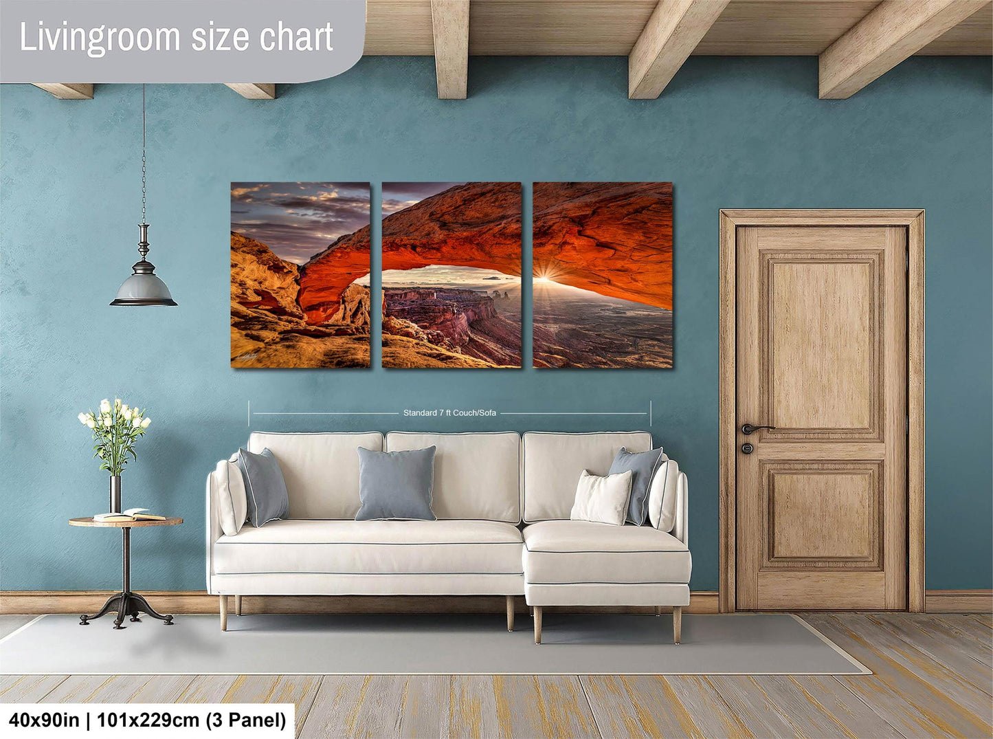 The image is a living room with a large, three-panel landscape painting hanging on the wall. The painting depicts a scenic view of a canyon with a red rock formation. The room has a white sofa and a wooden door, creating a cozy and inviting atmosphere.