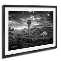 A black and white photograph of the Nashville skyline, featuring the iconic Space Needle and surrounding buildings, with a dramatic cloudy sky in the background.