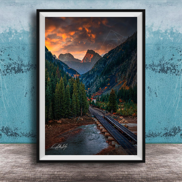 a scenic mountain landscape with a winding road, lush forests, and a dramatic sky with orange and red clouds.