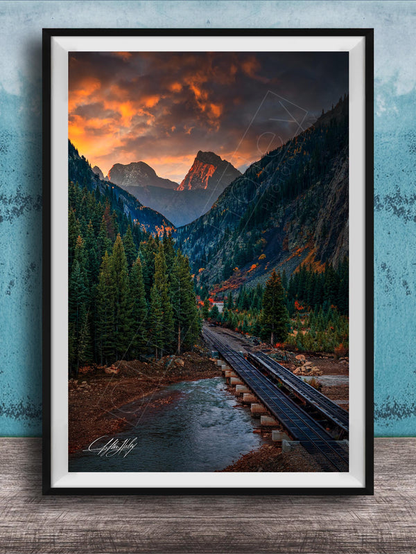 a scenic mountain landscape with a winding road, lush forests, and a dramatic sky with orange and red clouds.