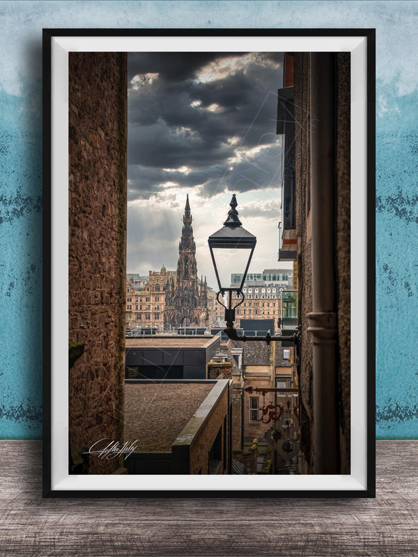 a cityscape with a tall, ornate building in the background, framed in a black frame and placed on a wooden surface against a blue wall.