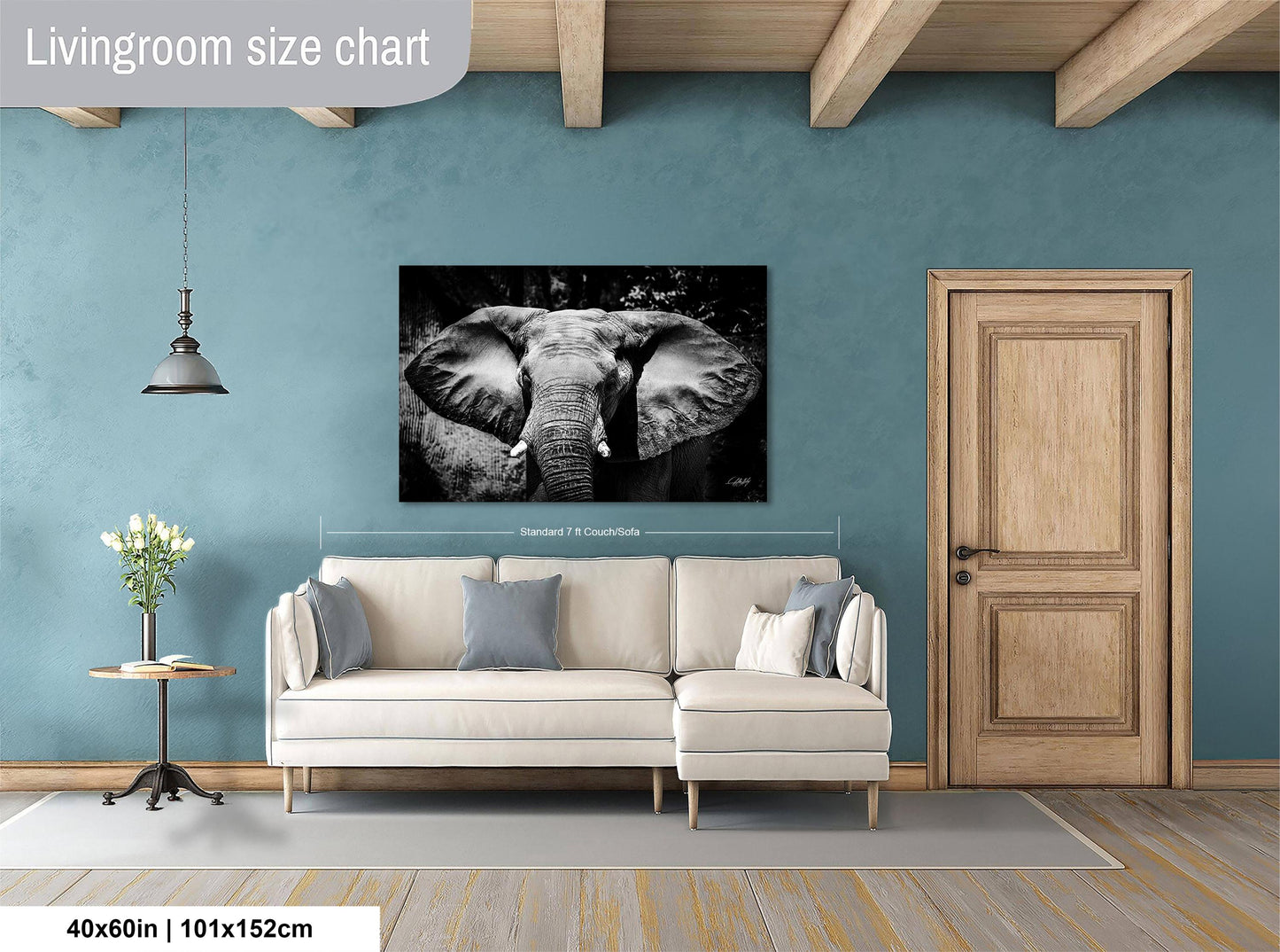 a living room with a large black and white elephant painting hanging on the wall. The painting is approximately 40 inches wide and 115 centimeters tall. The room has a white sofa, a wooden door, and a small table with a vase of flowers.